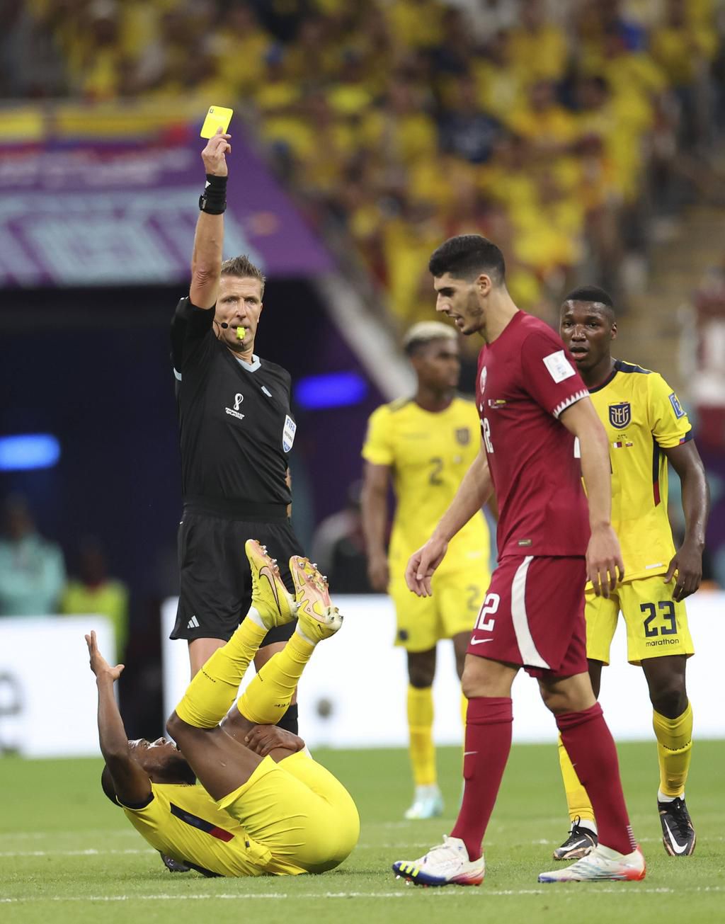 Referee Daniele Orsato (L) shows a yellow card to Qatar's Karim Boudiaf (Front R) after he tackled Ecuador's Enner Valencia (Bottom) during the Group A match between Qatar and Ecuador at the 2022 FIFA World Cup on November 20, 2022.
