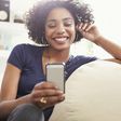 Smiling African American woman texting with cell phone on living room sofa