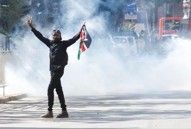A protester carries a flag of Kenya amid teargas fired by riot police during protests