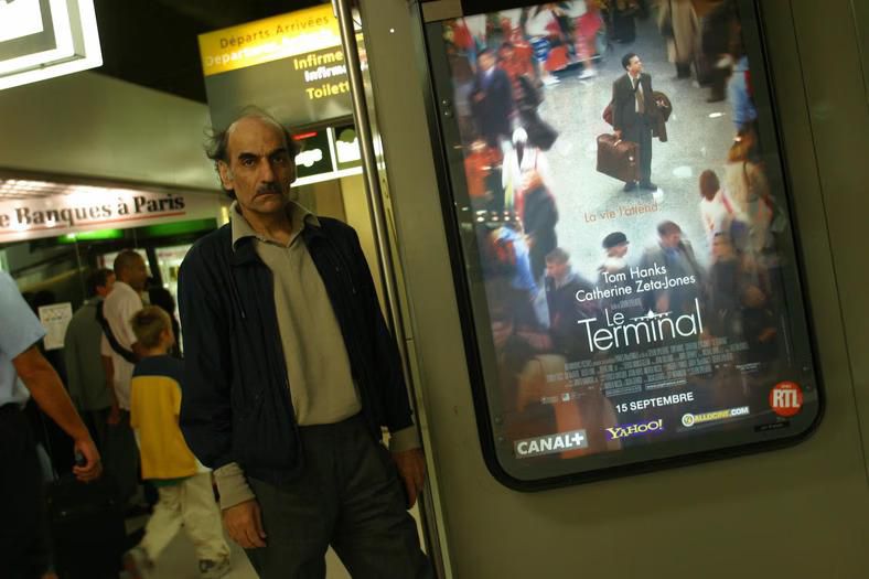 Mehran Karimi Nasseri next to the poster announcing the premiere of the film 'The Terminal' based on his life story [Getty]