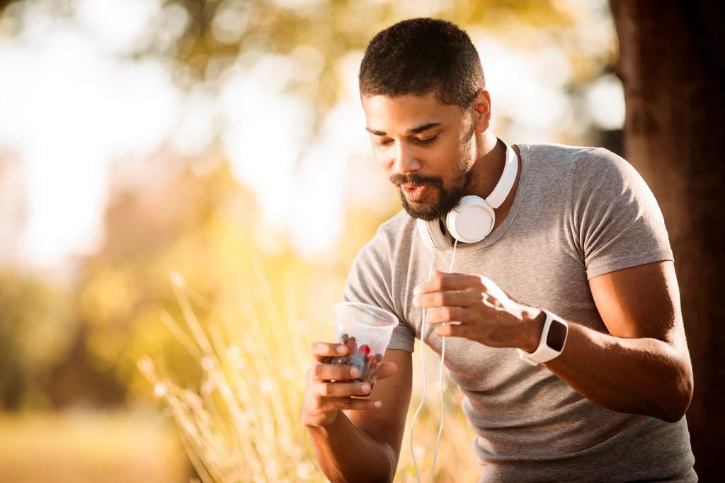 Active young man eating berries from a plastic cup in a public park