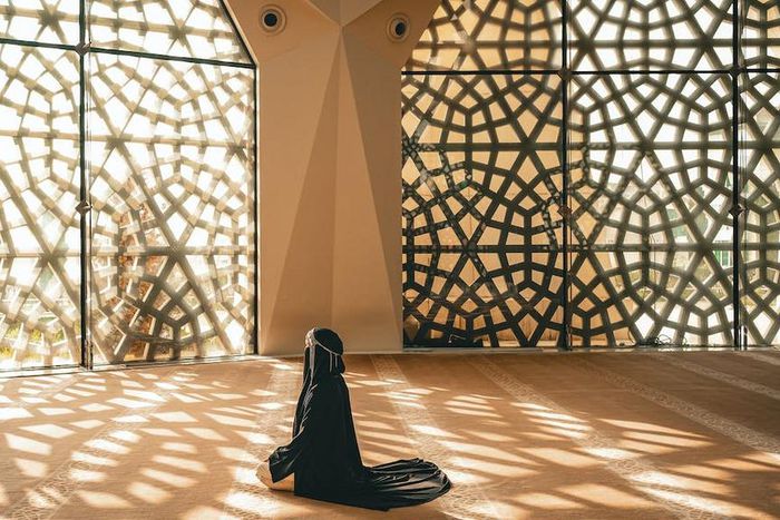 Woman praying in a mosque with openwork windows {image Credit: Hatice Baran]