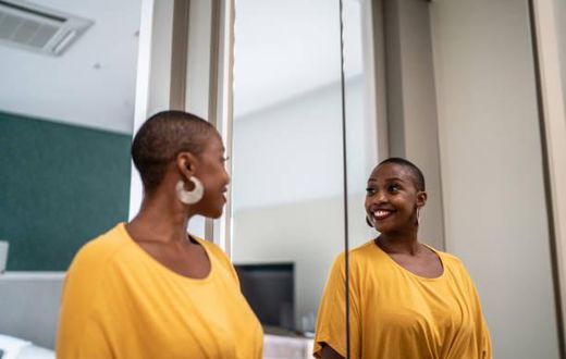 A Black woman looking in the mirror [iStock]