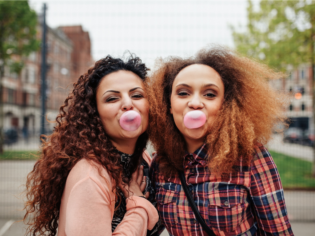 women chewing gum blowing bubbles happy hugging friends shutterstock_314302964
