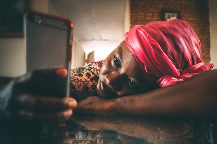 A woman in a headwrap and dera using her phone [Image Credit: Ekua Apau]