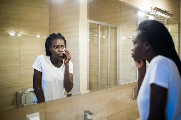 A Black woman looking in the mirror [Adobe Stock]