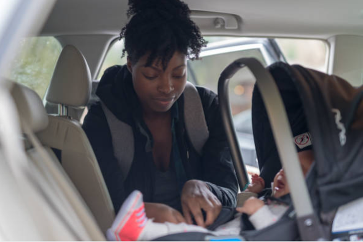 Mom puts her infant baby into a car seat [iStock]