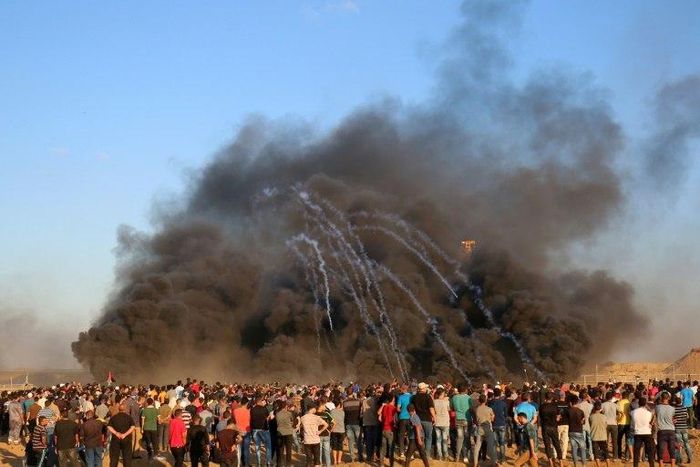 Palestinian protesters watch as tear gas canisters fired by Israeli forces comes through the black smoke of burning tyres during a demonstration on the Israeli border east of Gaza City on September 14, 2018
