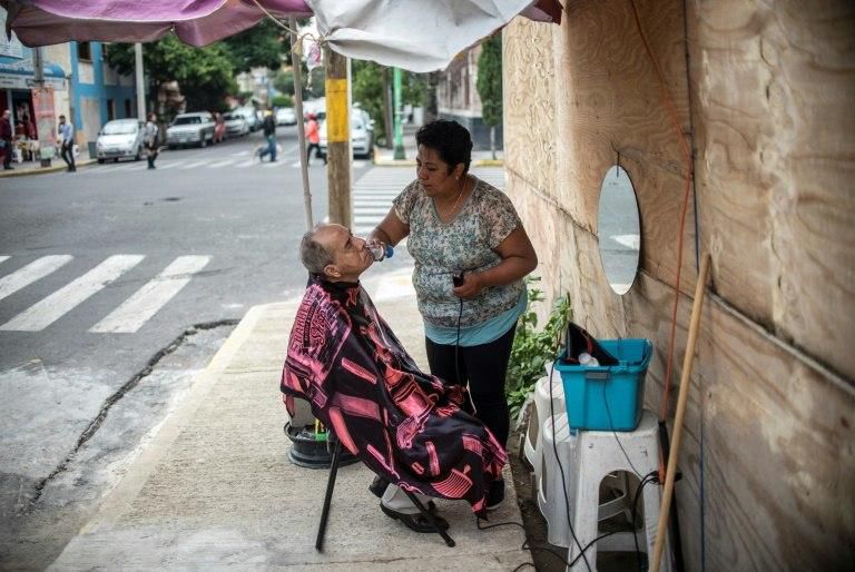 Stylist Xochilt de la Paz, who lost her mother and her business in the September 19, 2017 earthquake in Mexico City, works on a customers' stubble on the sidewalk in the city's Ninos Heroes neigborhood