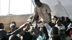 Des migrants se partagent une boisson dans de petites tasses