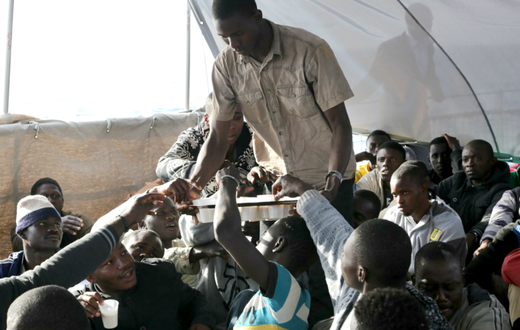 Des migrants se partagent une boisson dans de petites tasses