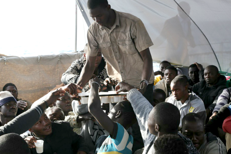 Des migrants se partagent une boisson dans de petites tasses