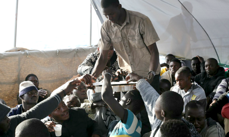 Des migrants se partagent une boisson dans de petites tasses