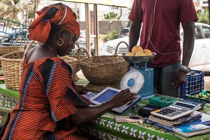 Une femme sur un marché de Dakar traite une commande de légumes à l’aide de sa tablette Weebi © Vincent Tremeau - La Banque mondiale