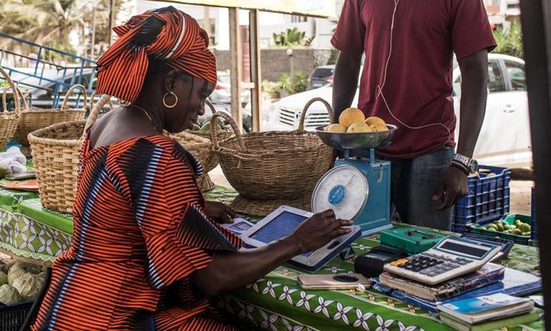 Une femme sur un marché de Dakar traite une commande de légumes à l’aide de sa tablette Weebi © Vincent Tremeau - La Banque mondiale