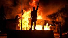 Un manifestant devant un bâtiment incendie dans la ville américaine de Minneapolis dans la nuit du 29 au 30 mai 2020