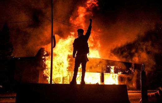 Un manifestant devant un bâtiment incendie dans la ville américaine de Minneapolis dans la nuit du 29 au 30 mai 2020