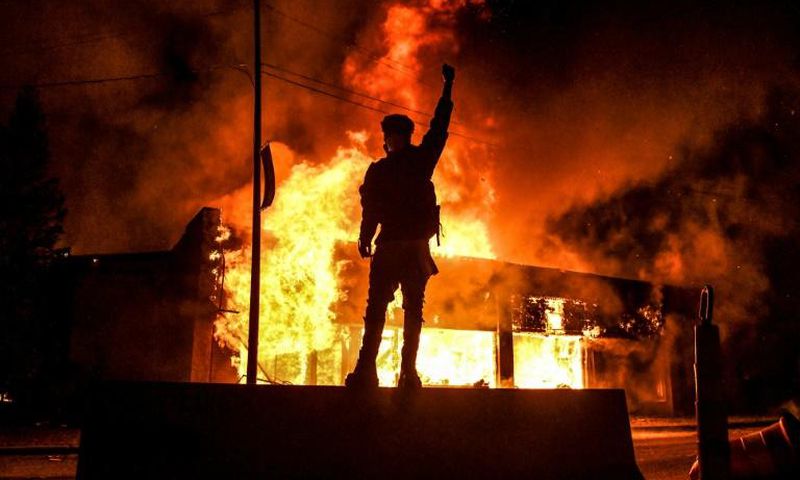 Un manifestant devant un bâtiment incendie dans la ville américaine de Minneapolis dans la nuit du 29 au 30 mai 2020