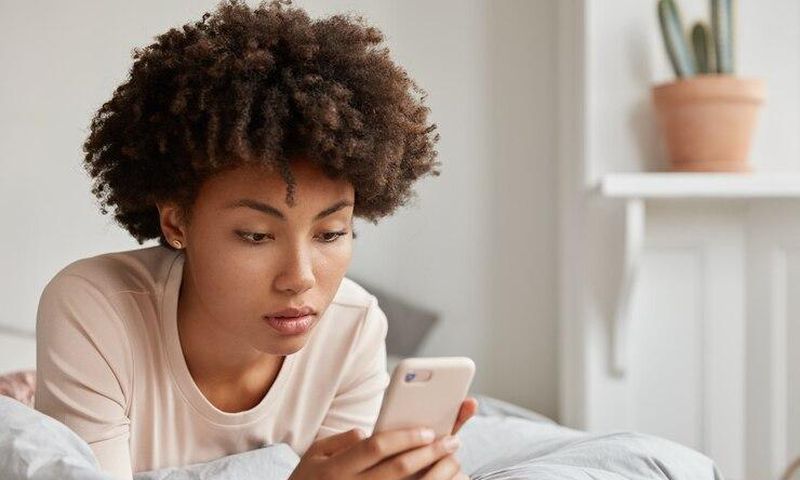 image-jeune-femme-noire-coupe-cheveux-afro-verifie-nouvelle-mise-jour-reseaux-sociaux-partage-fichiers-multimedias-son-telephone-portable-vetue-vetements-nuit-decontractes-se-repose-dans-son-lit-effectue-p