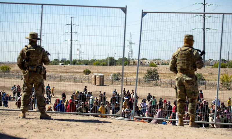 Migrants wait in line adjacent to the border fence under the watch of the Texas National Guard to enter into El Paso, Texas, May 10, 2023.Andres Leighton/AP Photo
