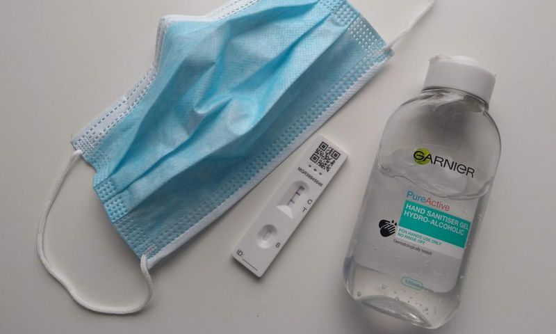 A face mask, a positive COVID-19 test, and a bottle of sanitizer.