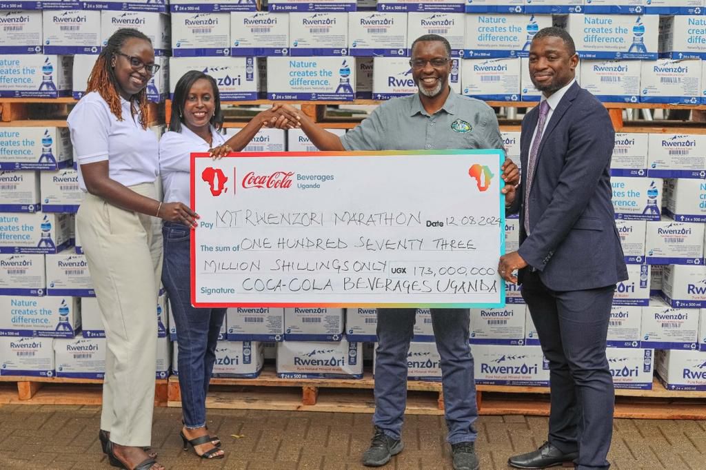 Pearl Nimusiima, the Public Affairs and Communications Manager of CCBU shakes hands with Amos Wekesa, the Tusker Lite Mt.Rwenzori Marathon  Team Leader  as she hands over a dummy cheque worth UGX 173m and boxes of Rwenzori  Pure Natural Mineral Water ahead of the Marathon