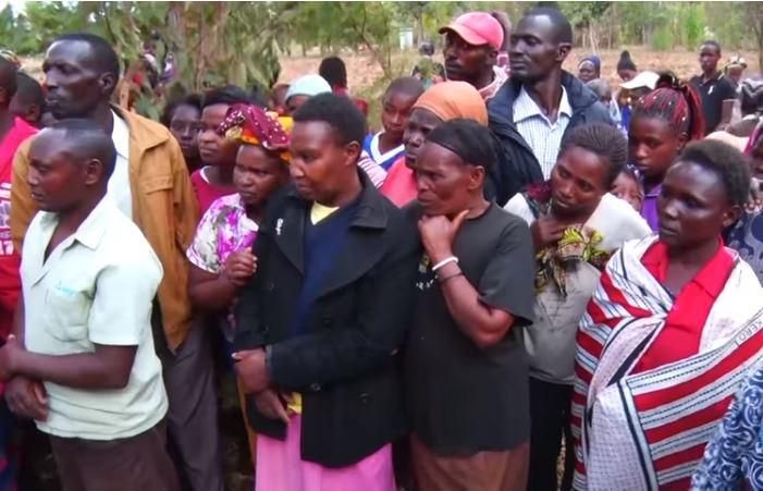 Residents watch in shock as police load the body of a woman who was hacked to death by her husband in suspected love traingle on to a vehicle