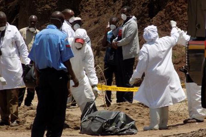 Detectives stabd next to the body of murdered Catholic priest Michael Kyengo