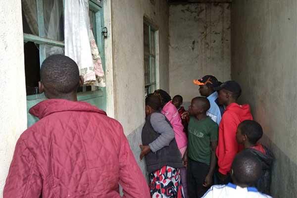Neighbours peep into the house where a man slashed his wife to death before hanging himself to death in Trans Nzoia
