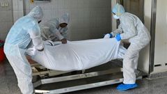 Employees lift the body of a COVID-19 victim before loading it into the furnace at the New Sonapur Hindu crematorium in Dubai