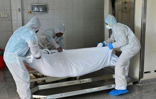 Employees lift the body of a COVID-19 victim before loading it into the furnace at the New Sonapur Hindu crematorium in Dubai