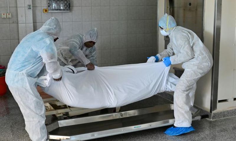 Employees lift the body of a COVID-19 victim before loading it into the furnace at the New Sonapur Hindu crematorium in Dubai