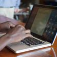 Black African man sitting at a restaurant typing on his laptop computer.