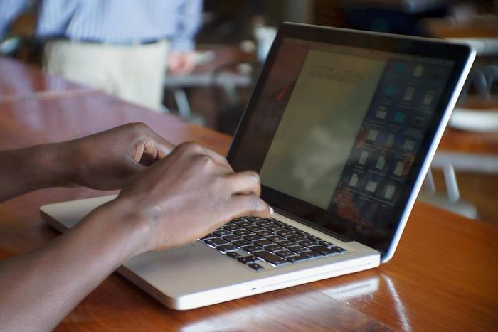 Black African man sitting at a restaurant typing on his laptop computer.