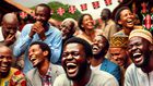 An AI-generated image of a lively scene depicting a black Kenyan man laughing loudly while using his smartphone, surrounded by a group of Kenyan people in a social gathering