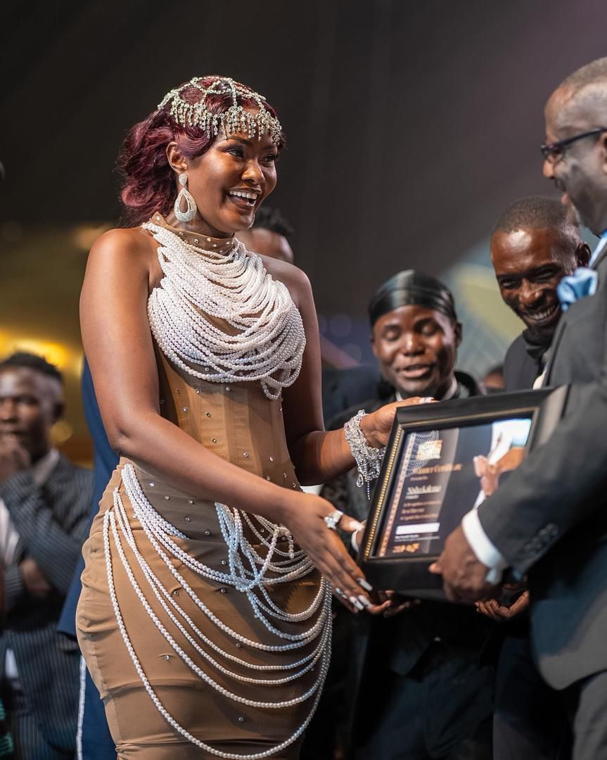 Nisha Kalema accepts a plaque from UCC's Nyombi Thembo at the awards