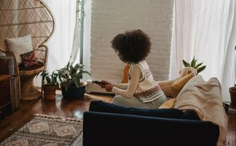 Focused young ethnic person with remote controller watching TV at home [Image credit: Andres Ayrton]