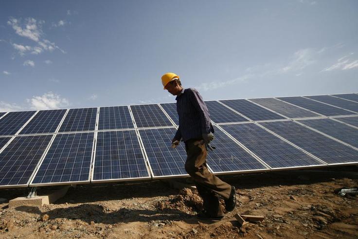 A construction worker walks past solar panels installed in Xinjiang, China.VCG /Getty Images