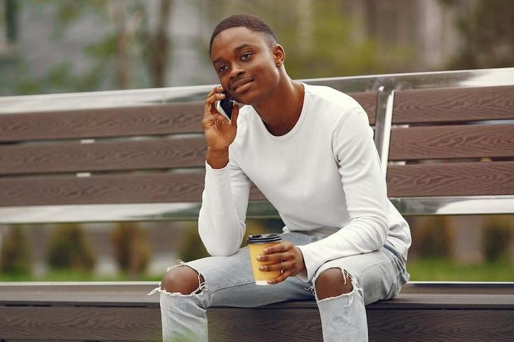 A young man using his phone while sitting on a park bench [Image: Gustavo Fring]