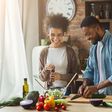Laughing black couple preparing salad in kitchen