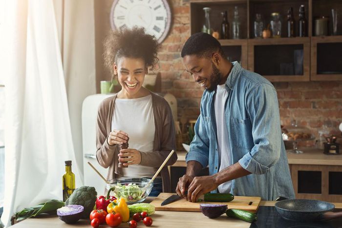 Laughing black couple preparing salad in kitchen