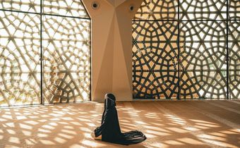 Woman praying in a mosque with openwork windows {image Credit: Hatice Baran]