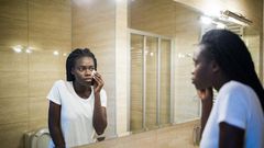A Black woman looking in the mirror [Adobe Stock]