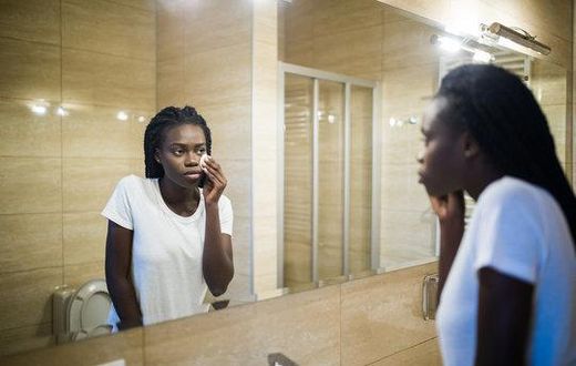 A Black woman looking in the mirror [Adobe Stock]