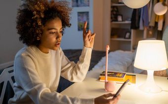 A teenager sitting on a desk while holding a phone [Image Credit: Cottonbro Studio]
