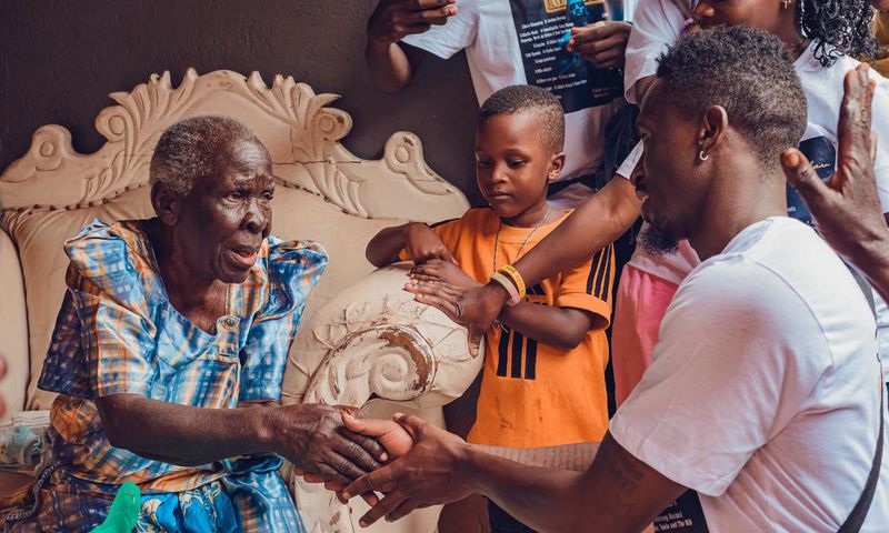 Rickman Manrick shakes hands with an elderly woman while in Bakuli, Kampala. Image credit: Bryan Morel Publications.