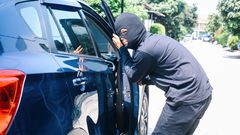 A photo of a masked man trying to enter into a car