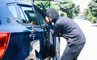 A photo of a masked man trying to enter into a car