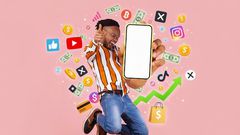An energetic young man jumps excitedly while holding up his smartphone. He is surrounded by a vibrant swirl of glowing social media icons (Instagram, TikTok, X, YouTube), gold coins, dollar signs, and upward-trending graphs.