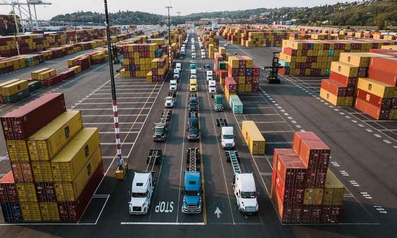 Parked trucks and cargo containers in a port [Image Creidt: Kelly]